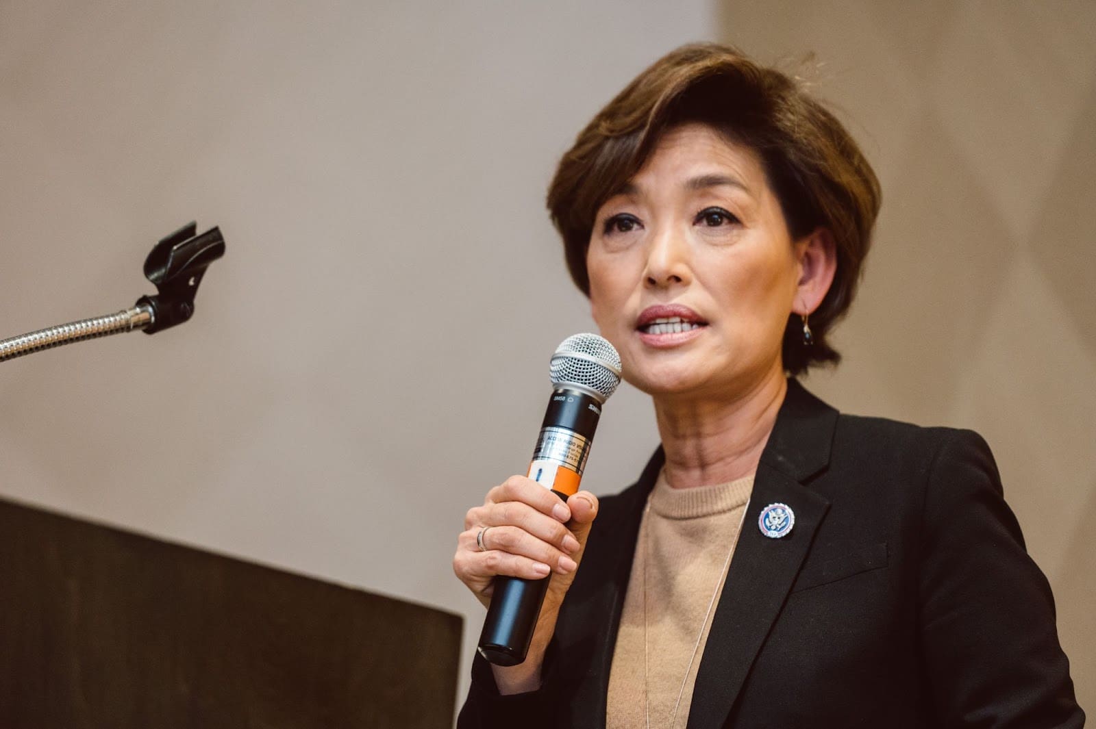 An Asian woman in a black suit holds a microphone.