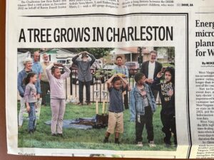The front page of a newspaper showing elementary-aged children with arms raised, standing around a newly planted tree