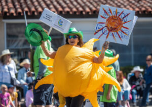 A woman wears an inflatable sun costume and holds a sign saying 'Sun Power'