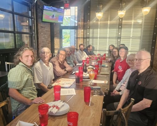 Smiling people sit at a long restaurant table in a casual dining setting