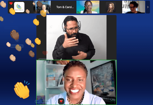 A Zoom screenshot shows a smiling Black woman with short hair. She's wearing a light blue shirt and a chunky gold necklace. An ASL interpreter is pictured above her, and there are clapping hands emojis of different colors filling the side of the screen.
