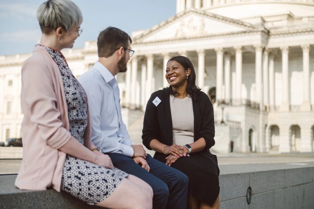 3 volunteers sitting in front of the U.S. capitol
