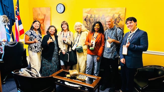 A diverse group of CCL Hawaii members stands shoulder to shoulder in a congressional office painted bright yellow